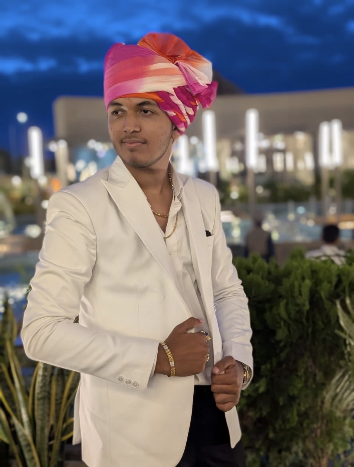 Divyarajsinh in white blazer and pink turban at a night event